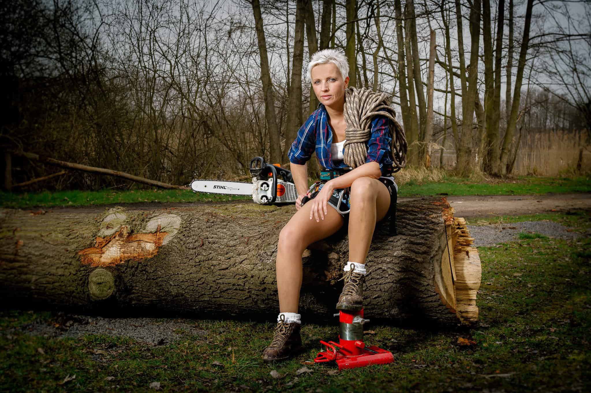 Frau mit Kettensäge und Kletterseil sitzt auf einem gefällten Baumstamm